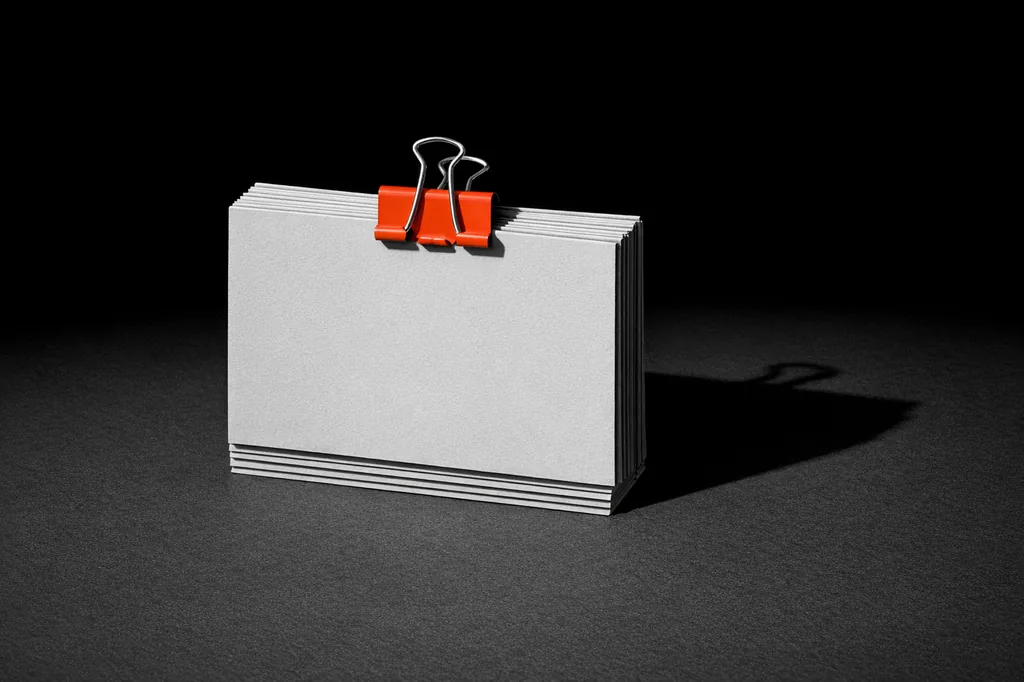 A stack of blank paper cards held together with a matte vermillion binder clip at the top, representing the eight-signal checklist